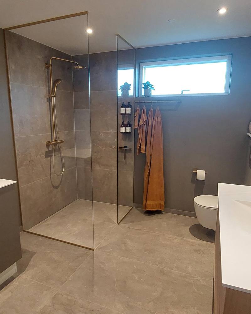 Badeværelse med grå fliser, glasvægge og armaturer i messing