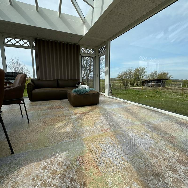 Udestue med mønsterklinker og panoramavinduer mod marken